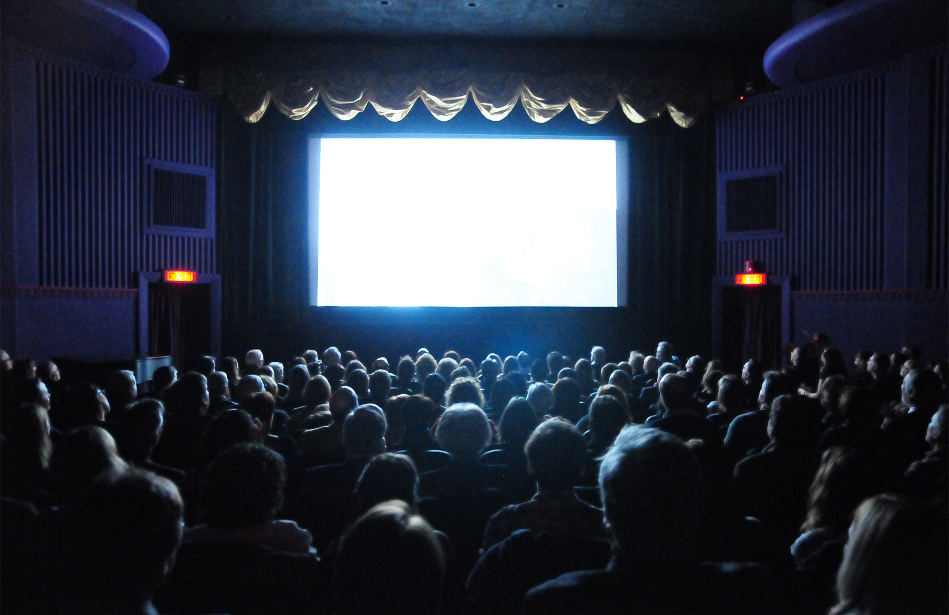 Movie theater with full audience and blank screen glowing in the dark