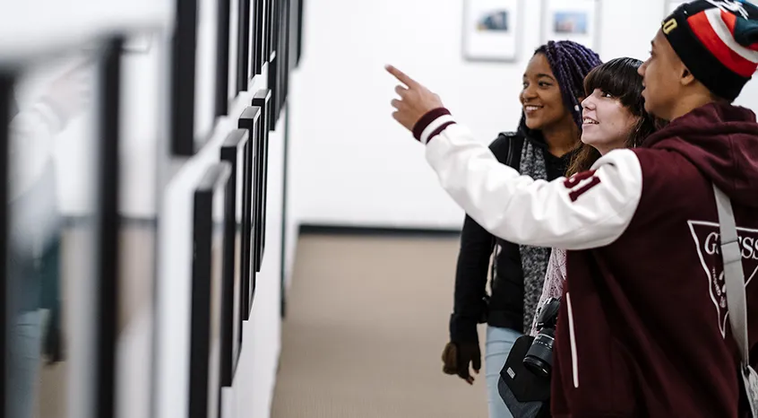 three young adults looking at framed photographs on gallery wall