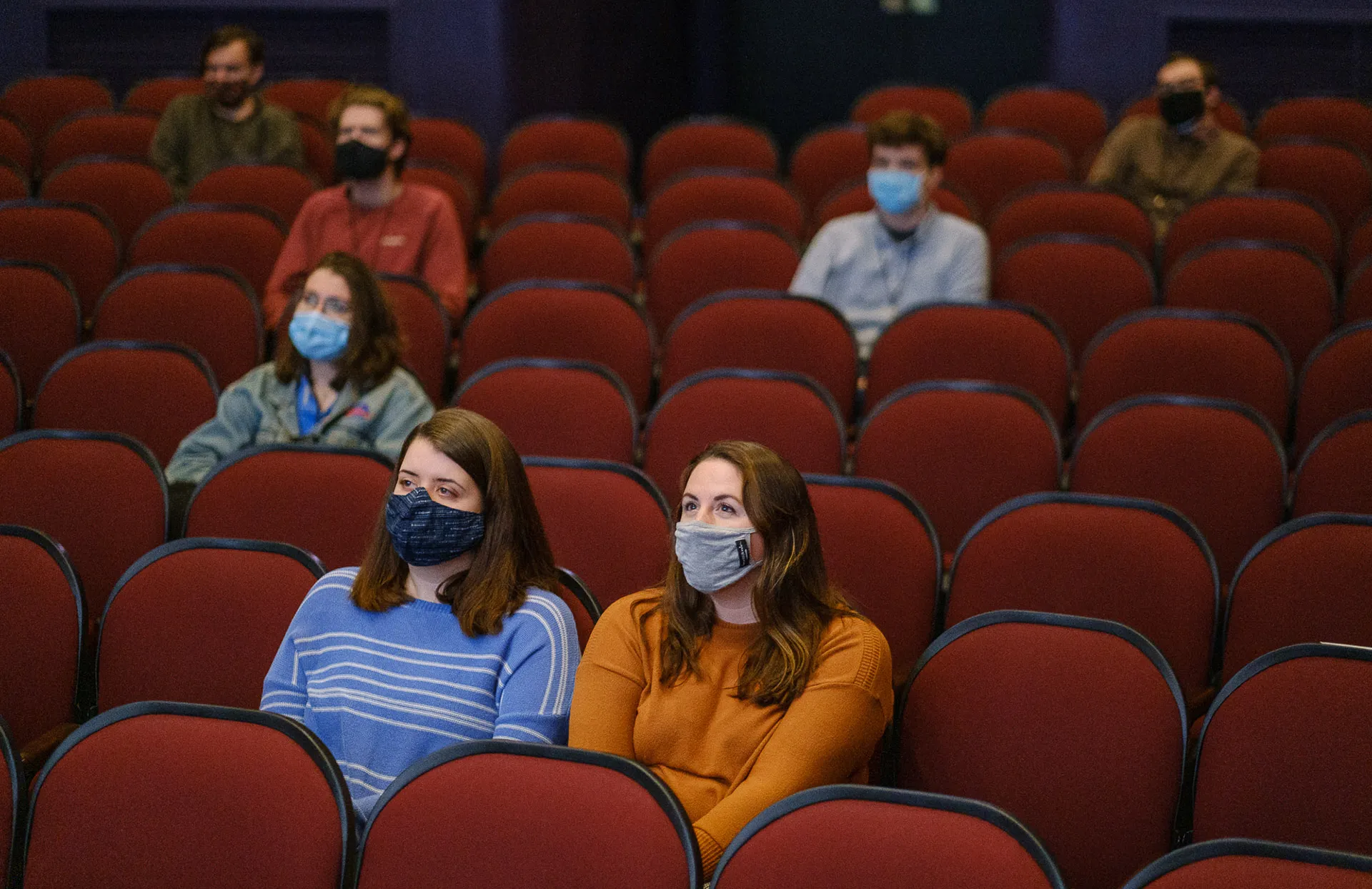 Seven adults wearing face masks sit spaced apart in theater seats 