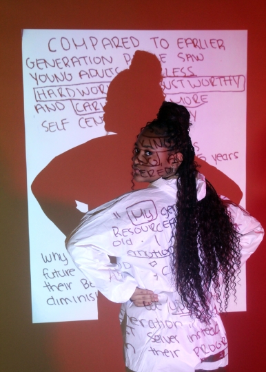 Young teenage girl of color in front of a projector discussing stereotypes as she looks at the viewers with her hands on her hips in red lights