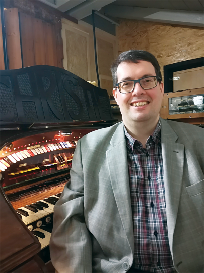 Headshot of Andreas Benz seated smiling at the camera next to an organ keyboard