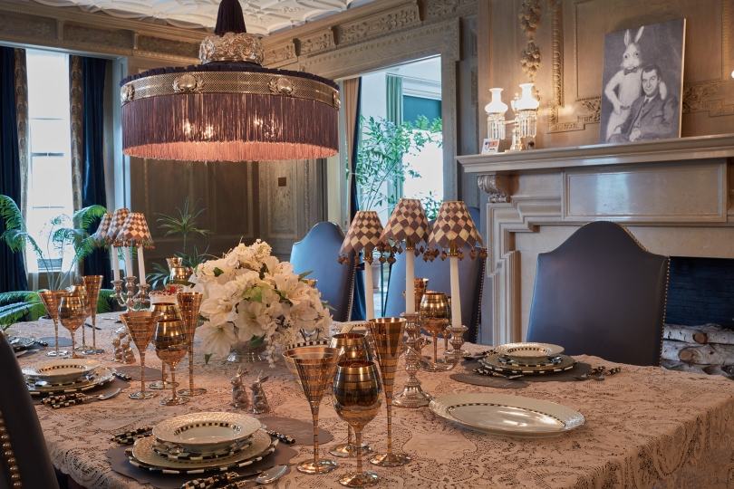Dining table decorated with glassware, china, and small rabbit figurines, with a portrait of James Stewart and a large rabbit from the movie Harvey on the mantel in the background