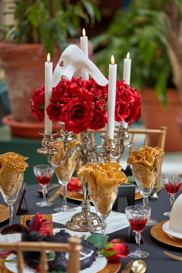 Table set with crystal glasses and china with a centerpiece of roses and a masquerade mask 