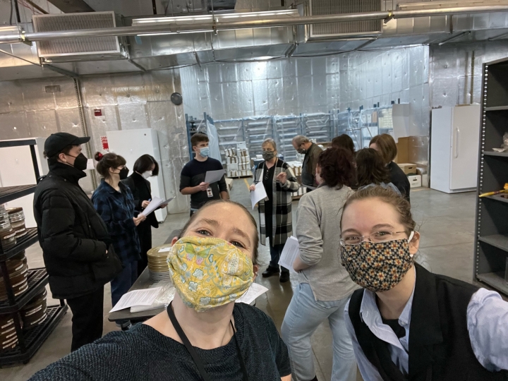 Selfie of Erica Jones and Lydia Creech in a film vault with group of people gathered around a table with film cans 