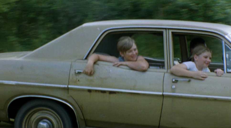 Two young children hanging outside an older vehicle 