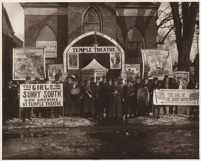 Group of people standing in front of Temple Theatre with signs advertising "The Girl of the Sunny South" 