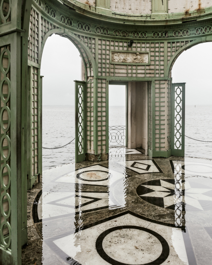 Ornate interior with body of water visible through three doorways and water over patterned marble floor