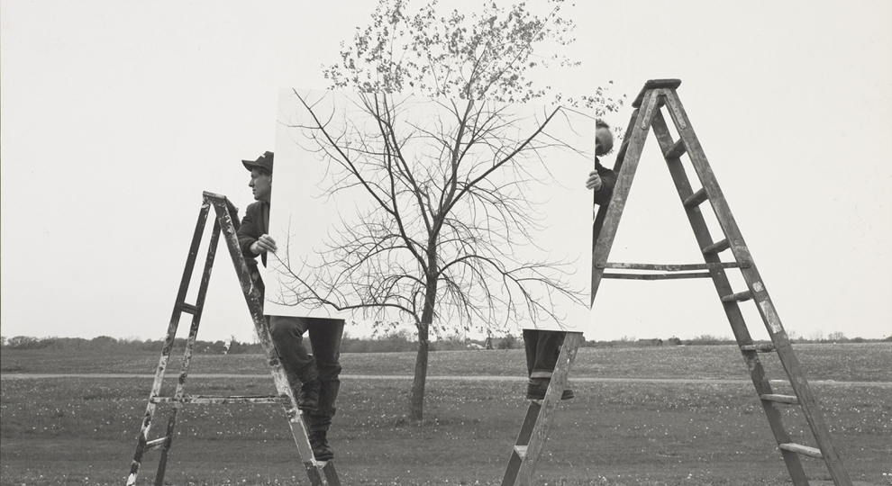 Photograph by JoAnn Verburg depicting two people on ladders holding up a photograph of a tree in front of a tree 