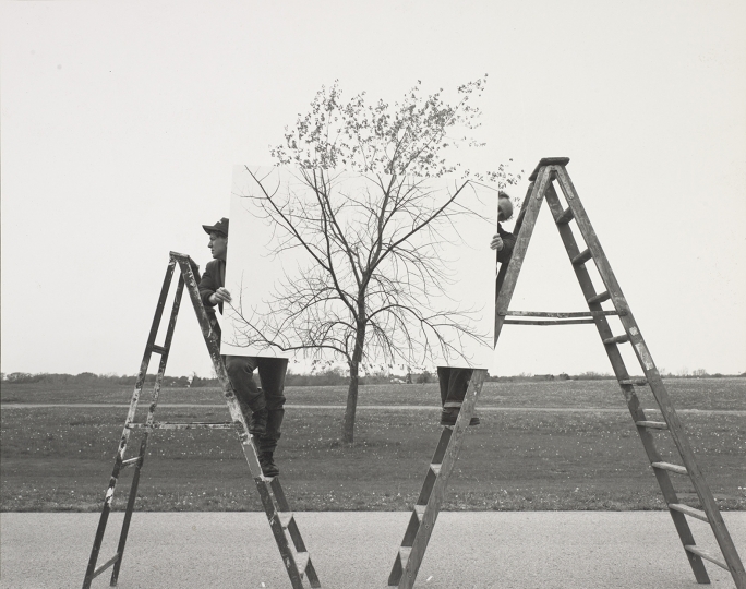 Photograph by JoAnn Verburg depicting two people on ladders holding up a photograph of a tree in front of a tree 