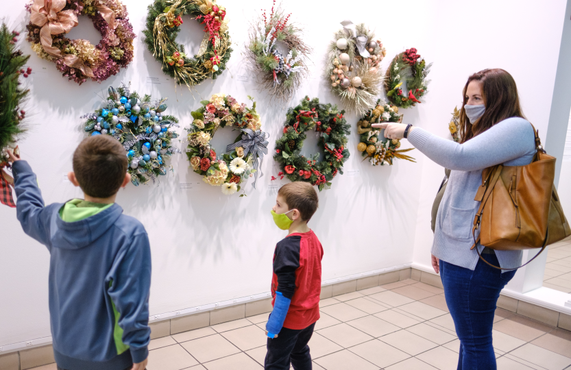 Two boys and a woman looking at wreaths