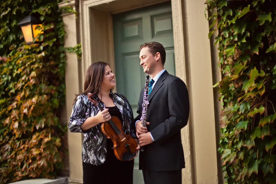A woman holding a violin and a man holding a clarinet in front of a door