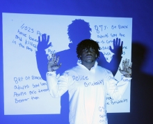 Young man of color with his hands up in front of a project that lists 