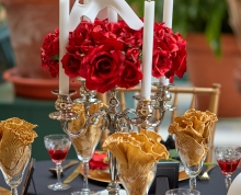 Table set with crystal glasses and china with a centerpiece of roses and a masquerade mask 