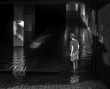 Dark interior of flooded parking garage with child seen from behind standing in water wearing a bicycle helmet