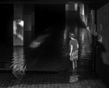 Dark interior of flooded parking garage with child seen from behind standing in water wearing a bicycle helmet