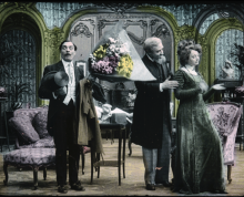 Painted original black and white film. Shows a surprised 19th c man holding flowers as an older man talks to a woman whose backs are turned.  