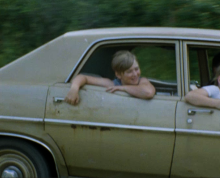 Two young children hanging outside an older vehicle 