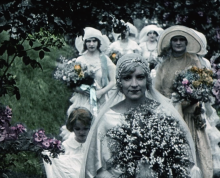 A hand painted film still that was black and white. A bride holds flowers with her procession behind her also holding flowers.
