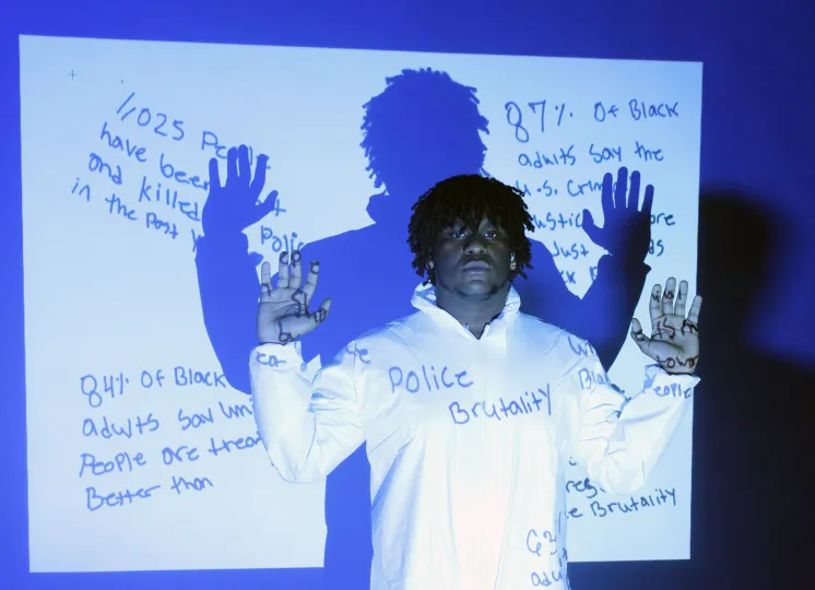 Young man of color with his hands up in front of a project that lists 