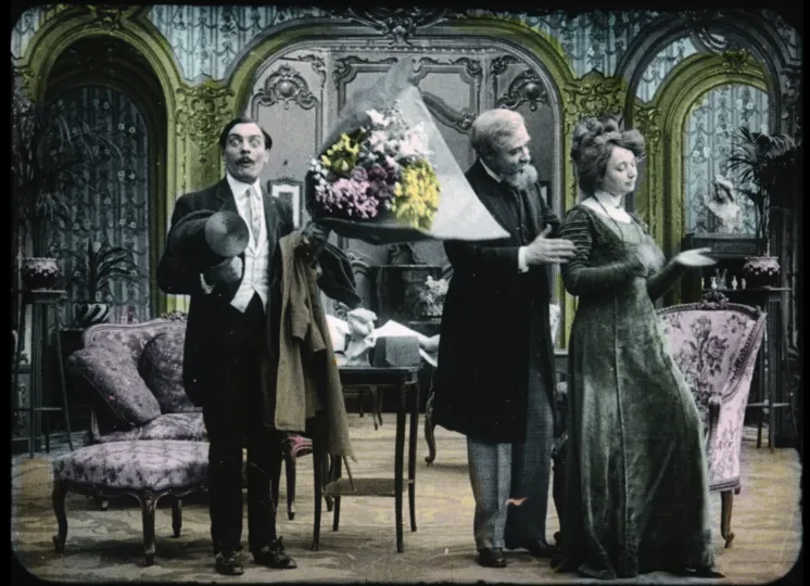 Painted original black and white film. Shows a surprised 19th c man holding flowers as an older man talks to a woman whose backs are turned.  