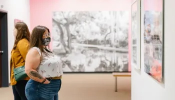 Two women looking at a work of art from one another - one woman is wearing a mask and the other is not