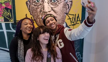 Group of young adults taking a selfie in front of a modern pop image of George Eastman