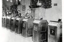 Three men among a line of eight Edison Kinetoscopes
