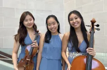 Three Asian women in dresses of the same color. One woman holds a violin, the woman in the center has no instrument, the woman on the end is holding a Cello