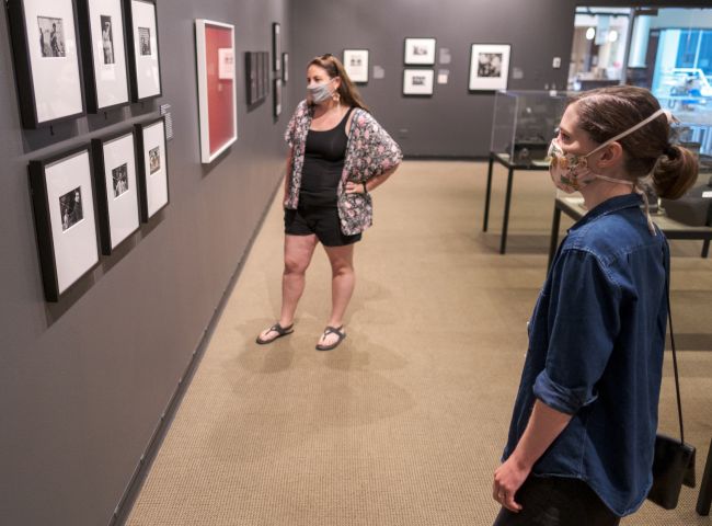 Two guests wearing masks looking at photographs in a gallery