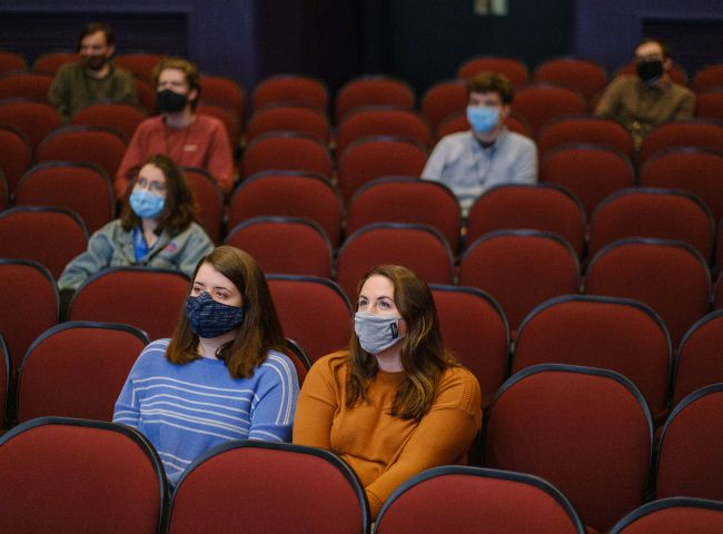 Seven adults wearing face masks sit spaced apart in theater seats 