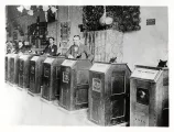 Three men among a line of eight Edison Kinetoscopes